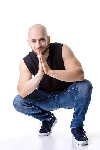 A German guy with shaved head squatting on the floor with clasped hands looking like his praying