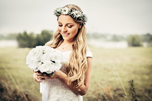 A blond smiling bride with a bouquet in a field