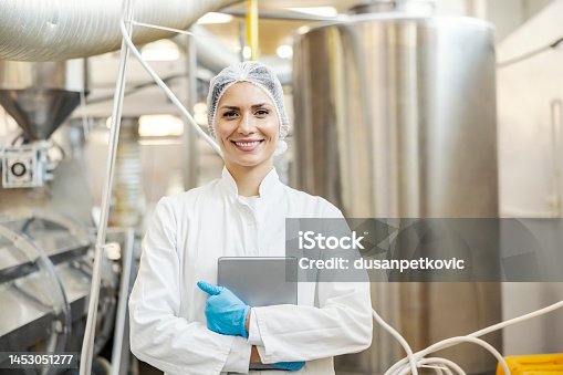istock A milk processing factory worker is standing in front of the tank with milk and holding tablet in her hands. 1453051277