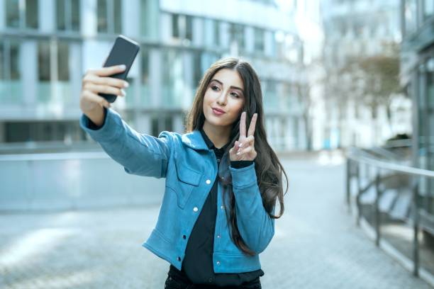 Beautiful teenager girl in city take selfie picture by smartphone in with fingers symbolize peace Beautiful teenager girl in city take selfie picture by smartphone in with fingers symbolize peace for followers at social media selfie girl stock pictures, royalty-free photos & images