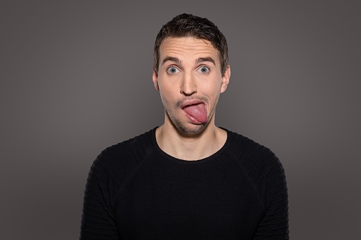 A closeup of crazy smiling man having fun while show his tongue and having a grotesque face with humor grimacing