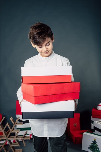 boy with tower of colored boxes in hands look to christmas presents standing in studio and have big expectations for unpacking