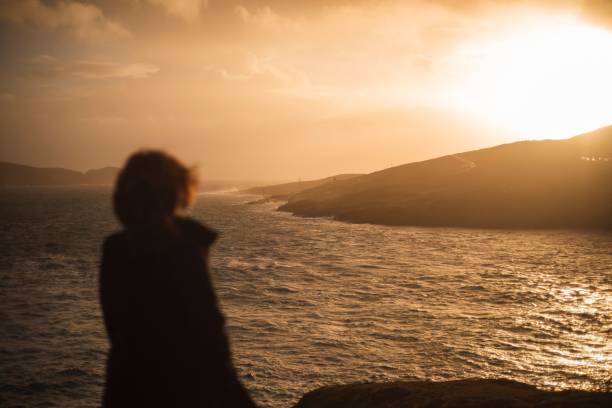 istock Back view of human standing and looking to sea during sunset 1453054505