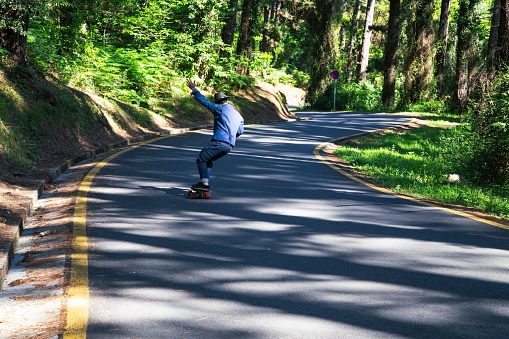 The view of a man skateboarding down the road through a forest