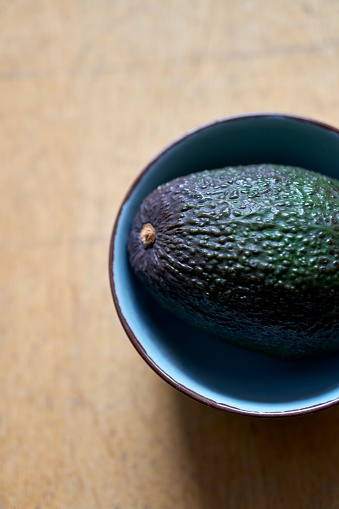 A top view of a fresh ripe avocado in a blue bowl on a wooden table