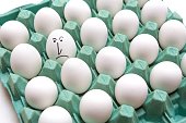 Closeup of an egg with a dissatisfied face in a carton of normal eggs