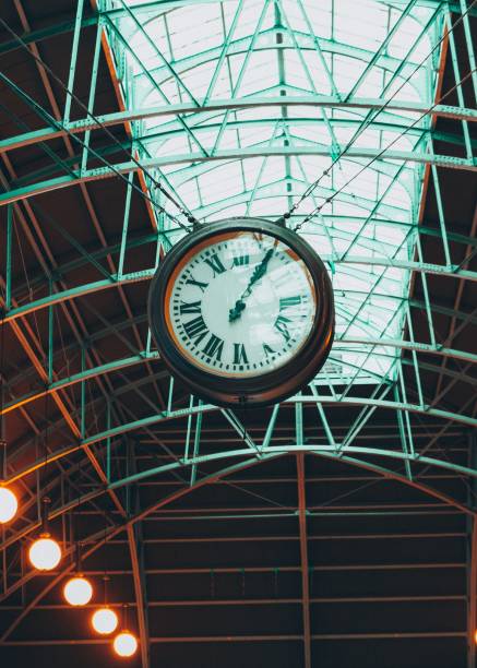 istock Vertical low angle shot of a clock hanging from a metal ceiling in a train station 1453058409