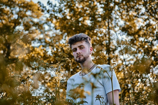A caucasian man staring at the camera through bushes in a forest