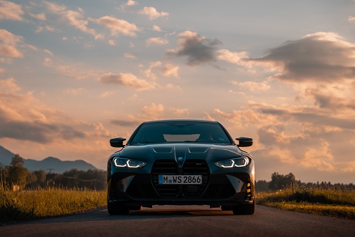Munich, Germany – May 21, 2022: Front view of a modern BMW M4 in the field during sunset with mountain v. Luxurious sports car is the dream car of many motorists
