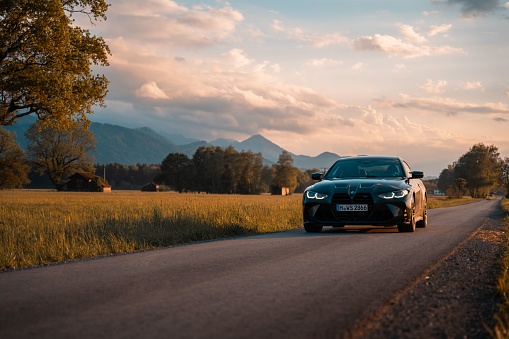 Munich, Germany – May 21, 2022: Front view of a modern BMW M4 in the field during sunset with mountain v. Luxurious sports car is the dream car of many motorists