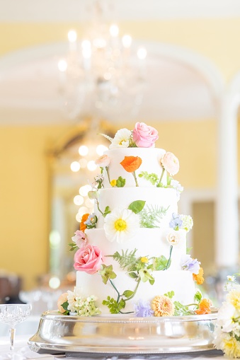 A vertical shot of a white multi layered wedding cake decorated with flowers in a beautiful hall