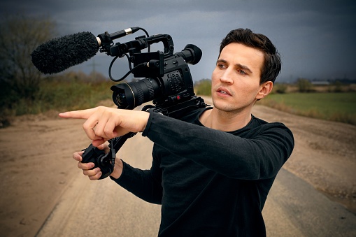 A young male cameraman with a camera pointing his finger to the side