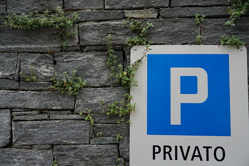 Parking lot shield with inscription in Italian language meaning private. The  shield is attached on a wall composed of stone blocks. Among the blocks grow creeping plants. Copy space is available.