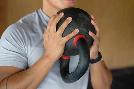 Close-up shot of  unrecognizable man holding kettlebell in front of his chest while doing strength training.