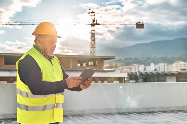 istock Middle aged bearded supervisor in hardhat and safety vest making notes in tablet on building site. Structural engineer or architect monitors progress of work on construction site. 1453066763