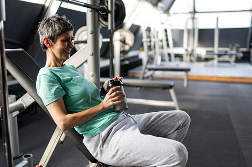 Mature woman with protein shaker sitting at gym after exercising