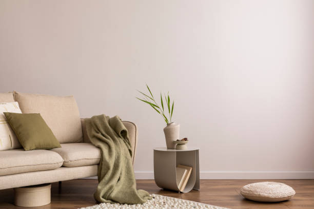 istock Interior design of living room with copy space, beige sofa, side table, leaf in vase, pouf, elegant accessories and boucle rug. Beige wall. Minimalist home decor. Template. 1453069045