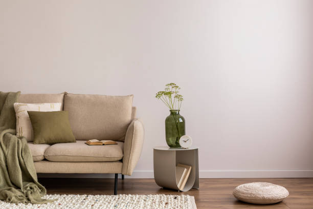 istock Interior design of elegant and outstanding space with copy spaace, beige sofa, coffee table, vase, green plaid and books. Beige wall. Copy space. Home decor. Template. 1453069092