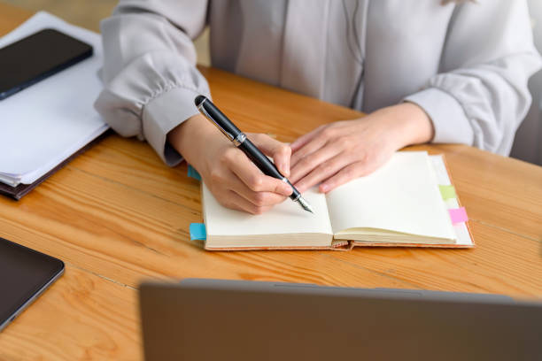 istock Close up image of a woman writing and taking note on notebook with laptop in office. 1453069504