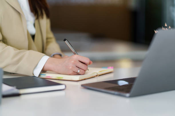 istock Close up image of a woman writing and taking note on notebook with laptop in office. 1453069623