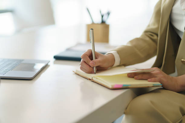 istock Close up image of a woman writing and taking note on notebook with laptop in office. 1453069625