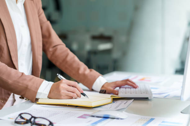 istock Close up image of a woman writing and taking note on notebook with laptop in office. 1453069658