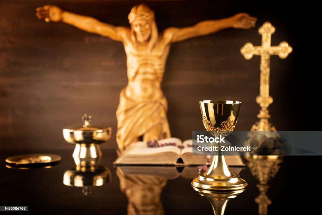 Catholic religion concept. Catholic symbols composition: cruciefied Jesus figure, The Cross, monstrance,  Holy Bible, rosary and golden chalice on brown background. Catholicism Stock Photo