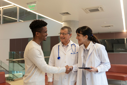 A senior male doctor and a young female doctor carrying a digital tablet are talking with an african american young patient's relative at a hospital waiting area