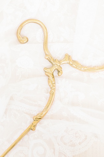 A vertical closeup shot of a golden vintage wedding hanger on a white textured fabric background