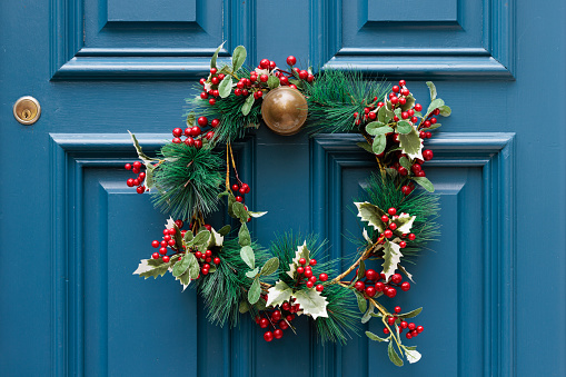 Decorative Christmas wreath on the Brass handle of a blue wooden door.