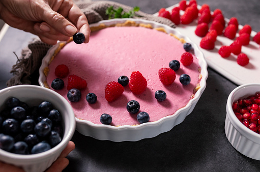 Blueberry and raspberry fruit pie. A woman decorates a fruit tart. Hands only