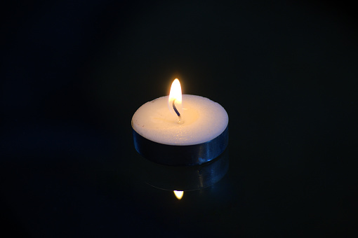 A blue and white birthday candle with a flame on black.