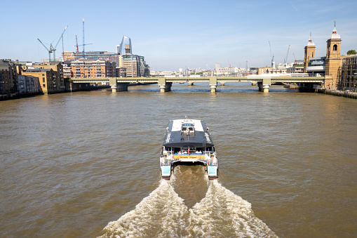 Cannon Street Railway Bridge. In the background is the skyline of the City of London including global architectural buildings. Passengers are visible on a tourboat.