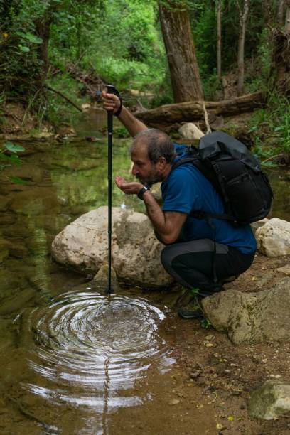 istock man with walking stick and backpack drinking water from a stream 1453104266