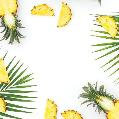 Sliced pineapples with palm leaves on white background. Tropical fruit frame. Flat lay, top view.