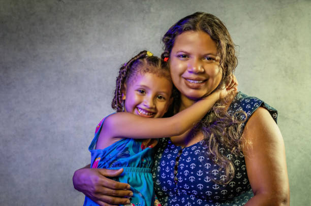 Braziliam mother and daughter hugging smiling for portrait, mom and child, black or brunette, studio portraits Studio portraits of a Brazilian mother, black or brunette, hugging her beautiful daughter with braids in her curly hair brazilian culture stock pictures, royalty-free photos & images