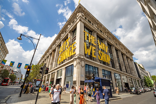 Tourists and shoppers walking past The Lets Change The Way We Shop sign on the exterior of Selfridges department store which is part of a project called Project Earth to accelerate the sustainability of its products.