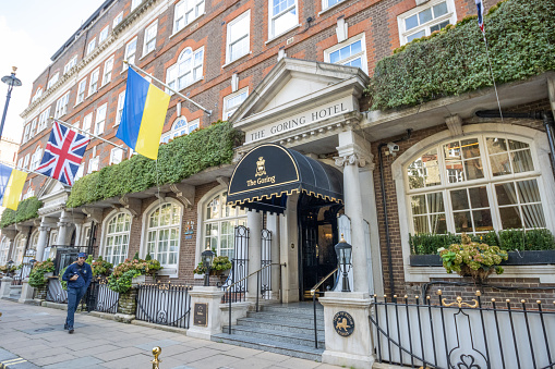 A man walks past Goring Hotel, with the Ukraine flag flying in sympathy  at the Russian invasion of February 2022. Built by Otto Goring in 1910, this luxury Edwardian hotel remains in the Goring family and is run by Jeremy Goring. The hotel has hosted the commander of the US expeditionary forces (World War I), an allied meeting held by Winston Churchill, and the Polish government in exile (both World War II). Kate Middleton stayed in the Royal Suite on the night of 28 April 2011, before her wedding to Prince William the next day. Meghan Markle and Prince Harry had a private lunch there in March 2020, the first time Meghan was seen back in the UK after the Megxit announcement.