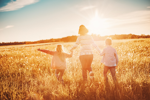 Mother with her children running on the field on the summer sunset. Concept of the family relationship and vacation.
