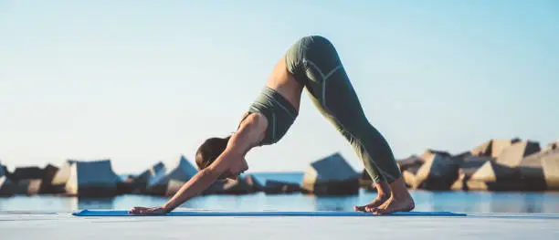 Photo of Shapely woman doing yoga in downward dog position near sea