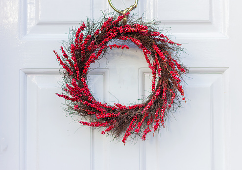 Christmas wreath of branches with red berries on a white wooden door, close-up