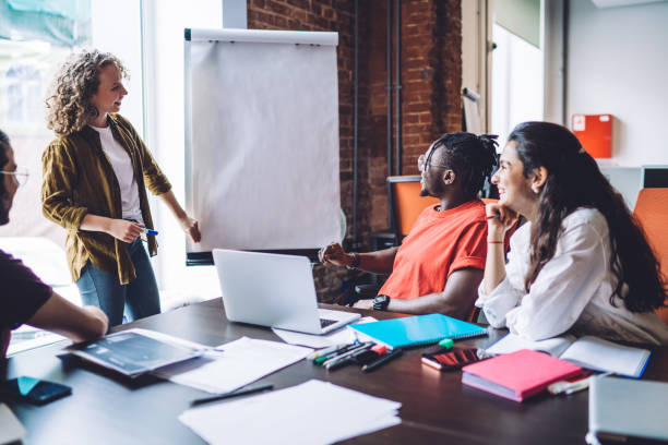 istock Young pleased employee giving presentation using white board to pensive diverse coworkers during work meeting in modern office 1453128282