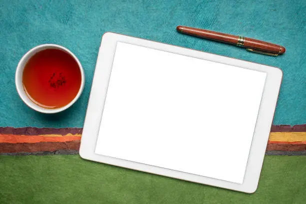 mockup of digital tablet with a blank isolated screen (clipping path included), flat lay with a cup of tea against abstract paper landscape