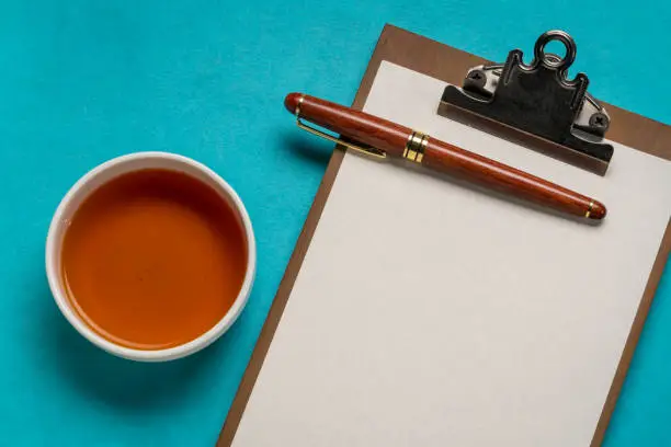 clipboard with a blank paper, desktop flat lay with a cup of tea and a stylish pen