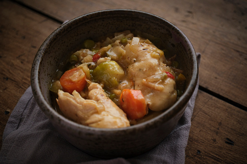 Bowl of homemade chicken and vegetable stew on a rustic wooden table.