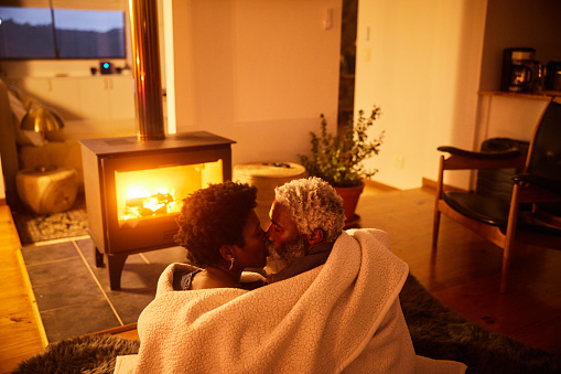 Loving couple kissing together wrapped in a blanket in front of a fireplace in their living room