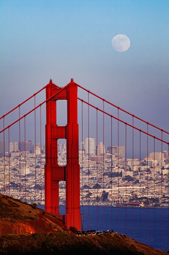 A vertical view of the tower of the Golden Gate Bridge with the San Francisco cityscape in the background