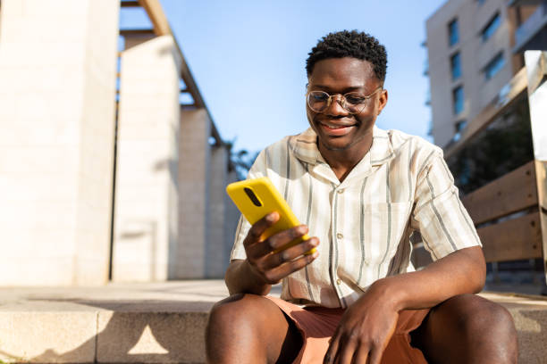 istock Young African American man using mobile phone outdoors sitting on stairs. Copy space. 1453135047