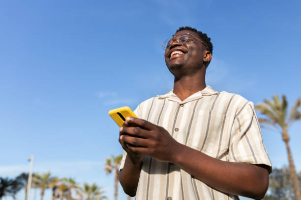 istock Happy black man laughing outdoors using mobile phone. Blue sky background. Copy space. 1453135272