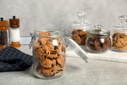 Delicious chocolate chip cookies in glass jars on light grey table